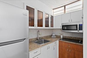 cocina con armarios blancos, fregadero y microondas en Beacfront Petite Paradise unit at Pelican Reef 103, en Rincón