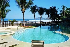 una piscina junto a una playa con palmeras en SecretJaco - Luxury Beach Front Penthouse with Pool & Jacuzzi, en Jacó