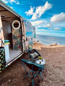 an rv with a table and a chair next to the ocean at On Road- feel freedom with campervan! in El Guincho