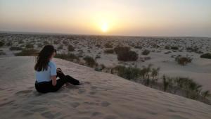a woman sitting on a sand dune watching the sunset at Private Camp25km-from DOUZ in Douz