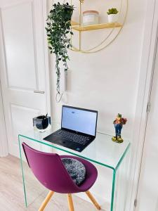 un computer portatile seduto su una scrivania in vetro con sedia viola di Central Derby Urban 2 Bedroom Flat - An Oasis of Elegance! Free Parking and Wifi suitable for families and professionals a Derby