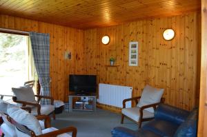 a living room with wooden walls and a tv and chairs at Reuben's Highland Retreat - Speyside in Carrbridge