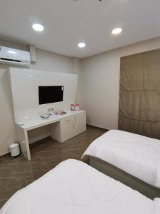 a room with two beds and a desk with a tv at Marina Town in Sohar