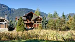 a large house with mountains in the background at Big Sky Chalet - Golf Course chalet, Hot Tub, Theatre, Scenic Views - Whistler Platinum in Whistler