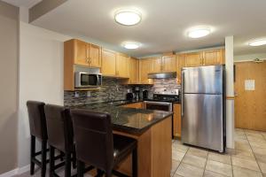 a kitchen with wooden cabinets and a stainless steel refrigerator at Woodrun Lodge 514 - Modern 1Bed + Den Condo with Pool, Hot Tub, Gym - Whistler Platinum in Whistler