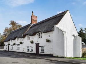 an old white building with a black roof at Richmond Cottage in Ashby Saint Ledgers