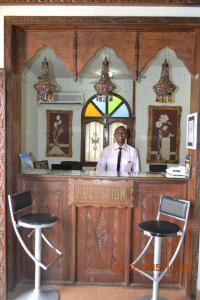 Un uomo in piedi in un bar con due sgabelli da bar. di Al-Minar Hotel a Zanzibar City