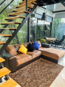 a living room with a brown leather couch with colorful pillows at Peaceful & Contemporary Duplex Escape in Ban Thap Nang