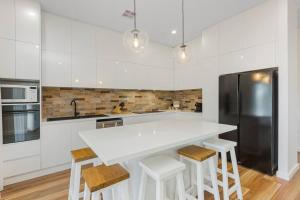 a white kitchen with a large white counter and stools at Cosy Retreat on Forest (Non Smoking) - Sleeps 6 in Bendigo