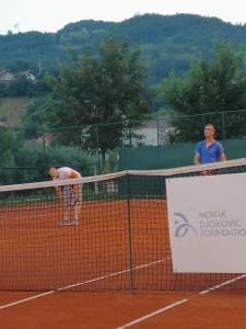 a man standing over the net on a tennis court at Apartmani River Priboj in Čitluk