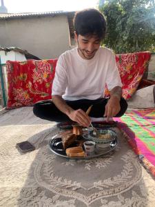 Guest house В гостях у Лаззат في Türkistan: رجل يجلس على بطانية مع صحن من الطعام