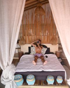 a man sitting on a bed taking a picture with a camera at La Beach Penida in Nusa Penida