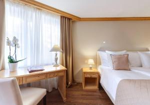 a bedroom with a bed and a desk and a window at Hotel Albatros in Zermatt