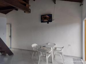 a white dining room with white chairs and a tv on a wall at Chalé do Saulo in Ilhabela