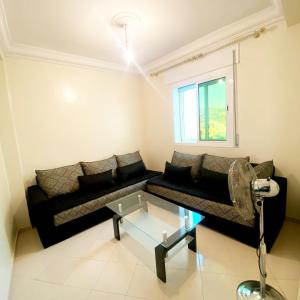 ein Wohnzimmer mit einem schwarzen Sofa und einem Glastisch in der Unterkunft Appartement Complète à Tanja balia proche de la mer in Tangier