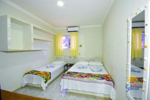 two beds in a small room with yellow curtains at Pousada Solmar in Japaratinga