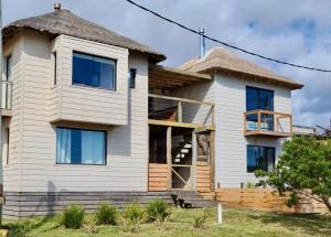 a large white house with a thatched roof at Cabañas 5 Sentidos in Punta Del Diablo