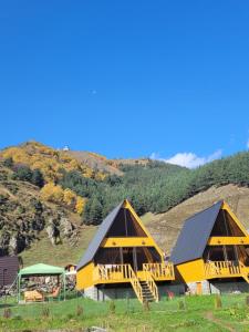 two large yellow buildings with a hill in the background at Pine Chalet Kazbegi in Stepantsminda