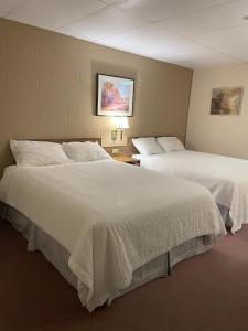 um quarto de hotel com duas camas com lençóis brancos em Rest Easy Motel em Three Hills