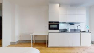 a white kitchen with white cabinets and a table at London City Apartment One in Ealing