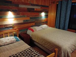 a bedroom with two beds and a wooden wall at Hostel Calafquen Coñaripe in Coñaripe