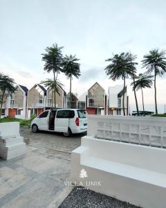 マランにあるVilla Unik Dau Malangのヤシの木が立ち並ぶ駐車場に停まった白いバン