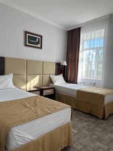 アクトベにあるTanzharyk Hotelのベッド2台と窓が備わるホテルルームです。