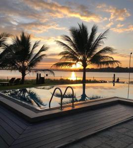 a swimming pool with two palm trees and a sunset at Hotel Lake Park in Polonnaruwa
