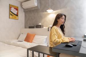 une femme assise sur un bureau avec un ordinateur dans l'établissement Uiwang Nine Hotel, à Uiwang