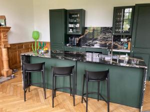 una cocina verde con taburetes negros en un bar en Maison MOKASSI, en Laloubère