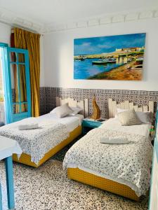 two beds in a room with a painting on the wall at Dar Evelyne in Mahdia