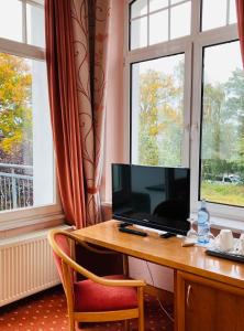 einen Schreibtisch mit einem TV und einem Stuhl in einem Zimmer mit Fenstern in der Unterkunft Hotel Germania in Bansin
