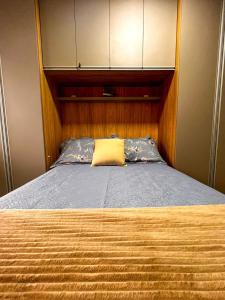 a bed with a wooden headboard and a yellow pillow at Seu refúgio a 250 metros do mar. in Governador Celso Ramos