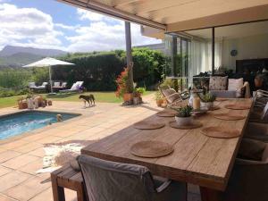 una mesa de madera en un patio con piscina en Lakeside home in security estate with solar power en Ciudad del Cabo