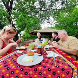 een groep mensen die aan een tafel eten bij Nje Bush Camp in Kwangwazi