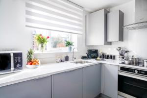 a white kitchen with a sink and a microwave at Spacious 4BR Townhouse Free Parking & WiFi in Milton Keynes