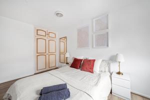 a white bedroom with a large white bed with red pillows at Arte Stays - 3-Bedroom Bright House London, Haggerston, Garden, Parking, 8 min walk to Haggerston Station, weekly or monthly stays, serviced accommodation - 7 guests in London