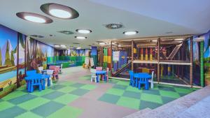 Grey Hotel Kopaonik في كوباونيك: غرفة لعب للأطفال مع أرضيات ملونة وطاولات وكراسي