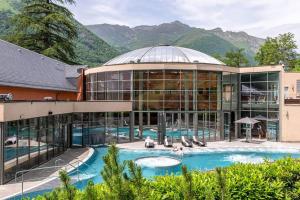a large building with a swimming pool with mountains in the background at Appartement plein Centre Cauterets, Vacances et Cures in Cauterets