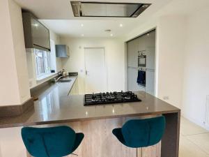 Il comprend une cuisine équipée d'une cuisinière et de 2 chaises bleues. dans l'établissement Modern new build detached House near Edinburgh Airport, à East Calder