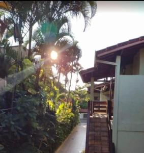 a house with the sun shining through the palm trees at Ape na Maranduba em frente à praia - Village 5 in Ubatuba