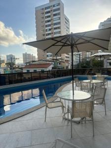 einen Tisch und Stühle mit einem Sonnenschirm neben einem Pool in der Unterkunft Surpreenda-se excelente apartamento com vista mar in Salvador