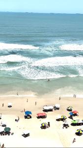 a beach with umbrellas and people in the ocean at Frente ao mar Pitangueiras - 3 suítes in Guarujá