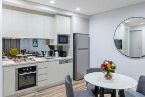 una cocina con armarios blancos y una mesa con sillas. en Meriton Suites Bondi Junction, en Sídney