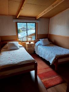 1 dormitorio con 2 camas y ventana en Hostal y Cabañas Ventisquero, en Puerto Puyuhuapi