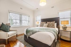 a bedroom with a bed and a chair and windows at Tranquil Inner-east Haven Moments from High Street in Melbourne