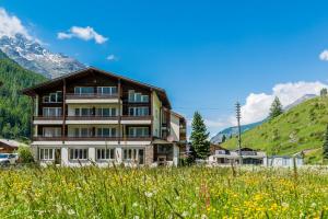 a building in a field with mountains in the background at Apartments Atlas in Saas-Grund