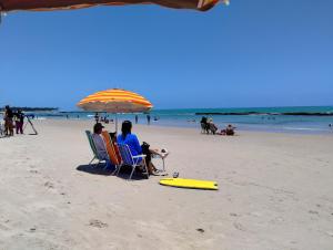 twee mensen zitten in stoelen onder een parasol op het strand bij Casa em Tamandaré a 1km de Carneiros no Condomínio Cote d' Azur in Tamandaré