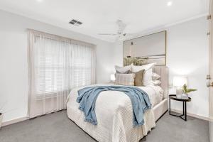 a white bedroom with a bed with a blue blanket on it at Waves and Walks - Close to Beach and Local Boutiques in Glenelg