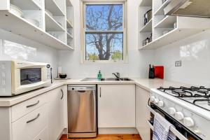 Il comprend une cuisine blanche équipée d'une cuisinière et d'un four micro-ondes. dans l'établissement East Parklands Cottage - A Dreamy Garden Hideaway, à Adélaïde